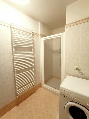 A bathroom with a shower, a radiator, and a washing machine.