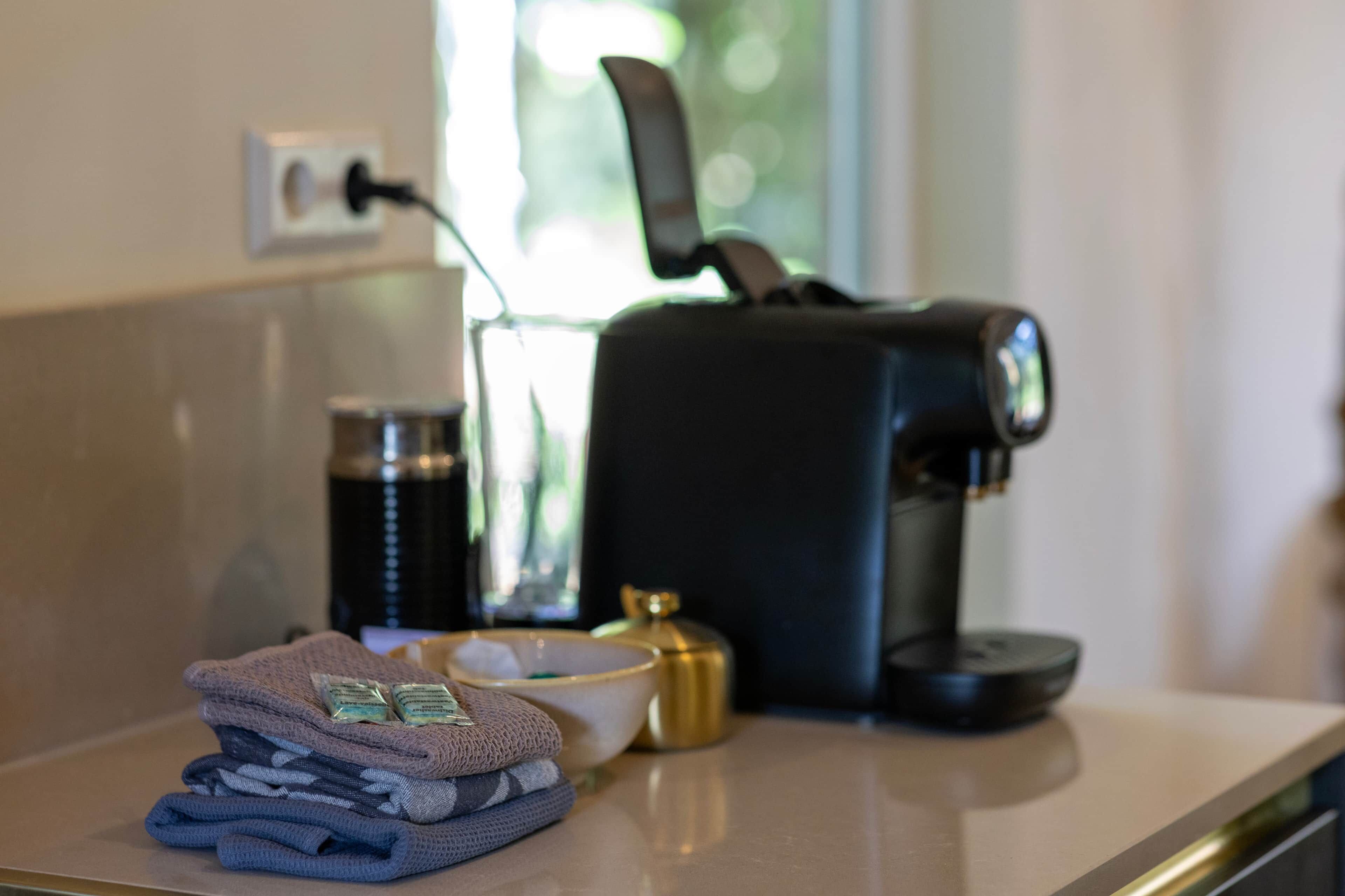 Una encimera de cocina con cafetera, una botella y toallas dobladas.