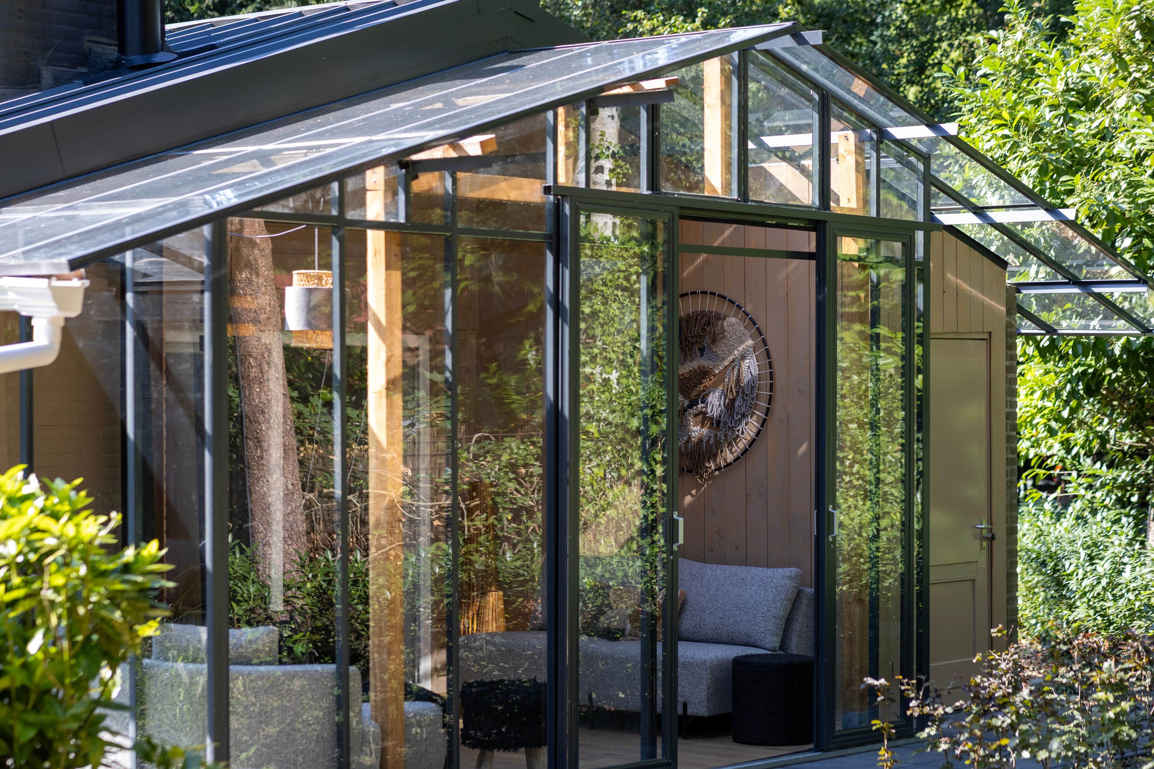 Ein Wintergarten mit Glasdach, Holzwänden und einer Sitzecke mit Kissen.