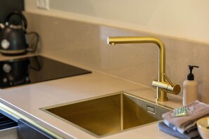 Eine Küche mit einer Spüle aus Edelstahl, einem Wasserhahn, einer Seifenspender und einem Wasserkocher auf der Arbeitsfläche.