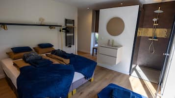Ein modernes Schlafzimmer mit Bett, Nachttischen, einem Einbauschrank, einem Badezimmer mit Dusche und einem großen Fenster.
