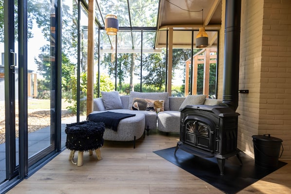 A modern living room with a fireplace, a sofa set, and a large window offering a view of the outdoors.