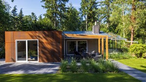 A modern house with a glass door entrance, a patio with outdoor seating, and a well-maintained garden. - ZEN-Bungalow no 7 with Forest serre, sauna and hottub (Rheezerveen)