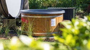 A wooden hot tub with a warning sign, surrounded by greenery and a tree. - ZEN-Bungalow no 7 with Forest serre, sauna and hottub (Rheezerveen)