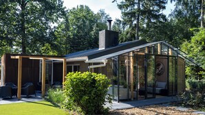 A modern house with a glass conservatory, a patio with outdoor furniture, and a well-maintained lawn. - ZEN-Bungalow no 7 with Forest serre, sauna and hottub (Rheezerveen)