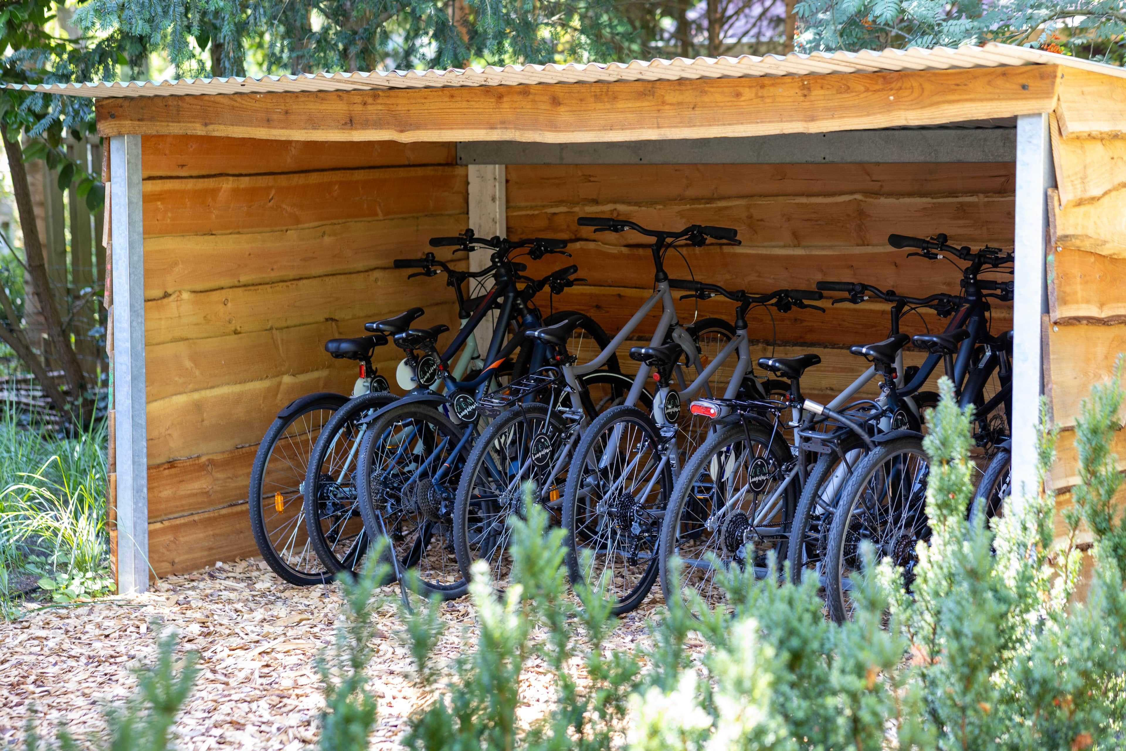 A wooden structure with a corrugated roof, housing multiple bicycles.