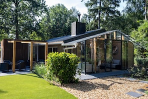A modern house with a glass conservatory, a patio with outdoor furniture, and a well-maintained garden.