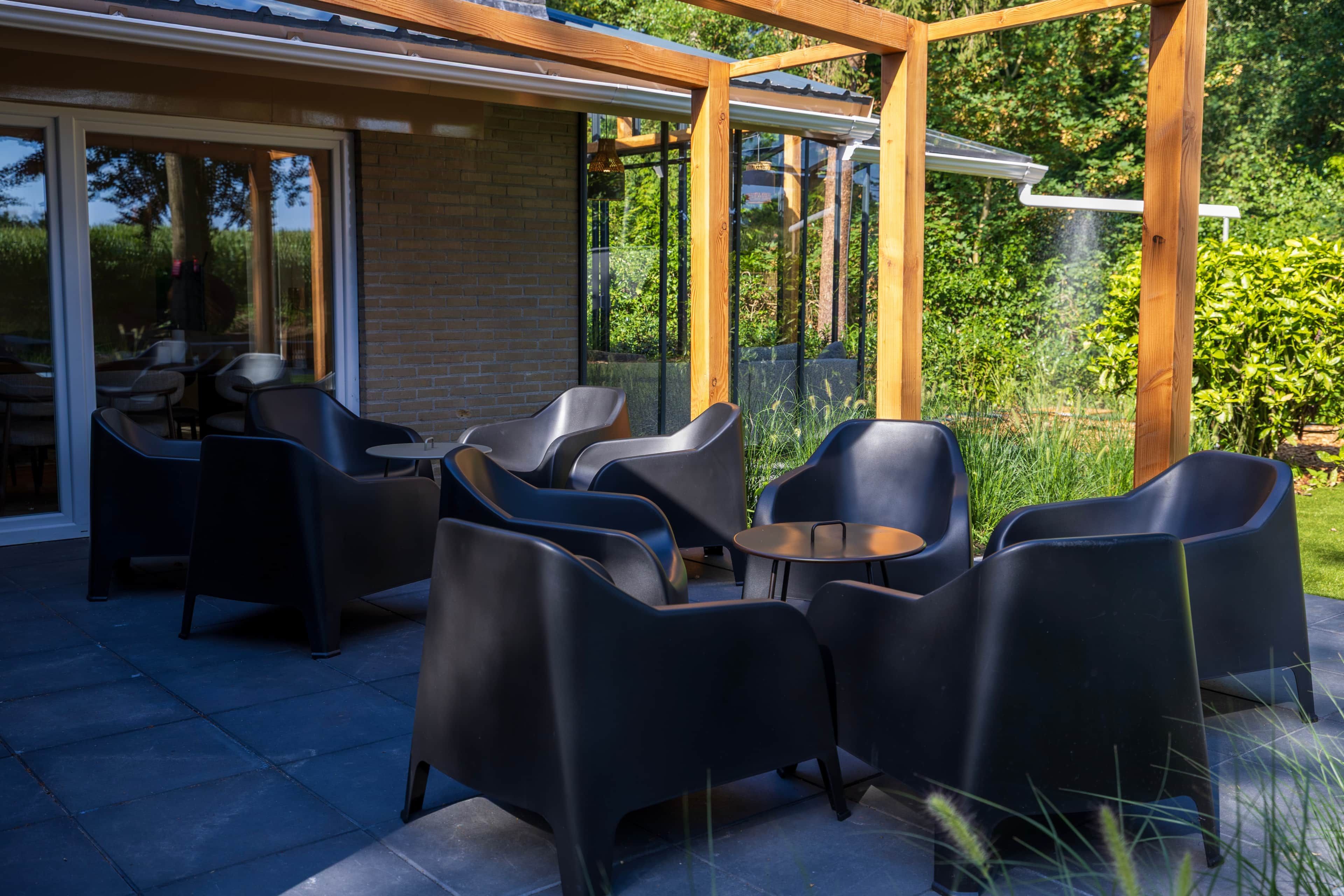 An outdoor patio area with a wooden pergola, black chairs, and a table.