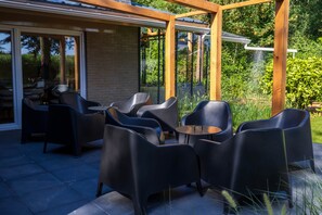 Un patio al aire libre con una pérgola de madera, sillas negras y una mesa.