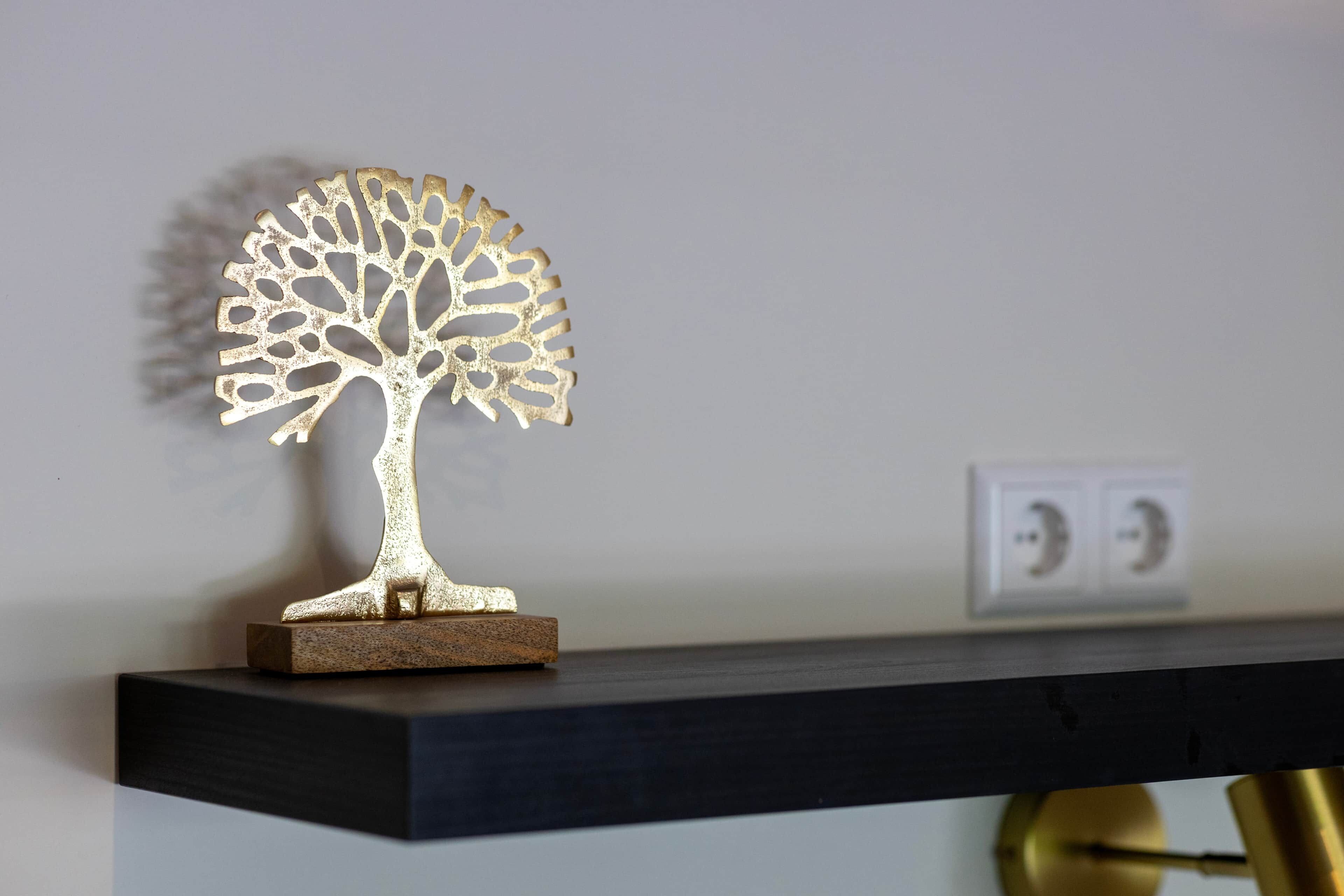 Una scultura di un albero in metallo su un ripiano di legno scuro, di fronte a una parete liscia.