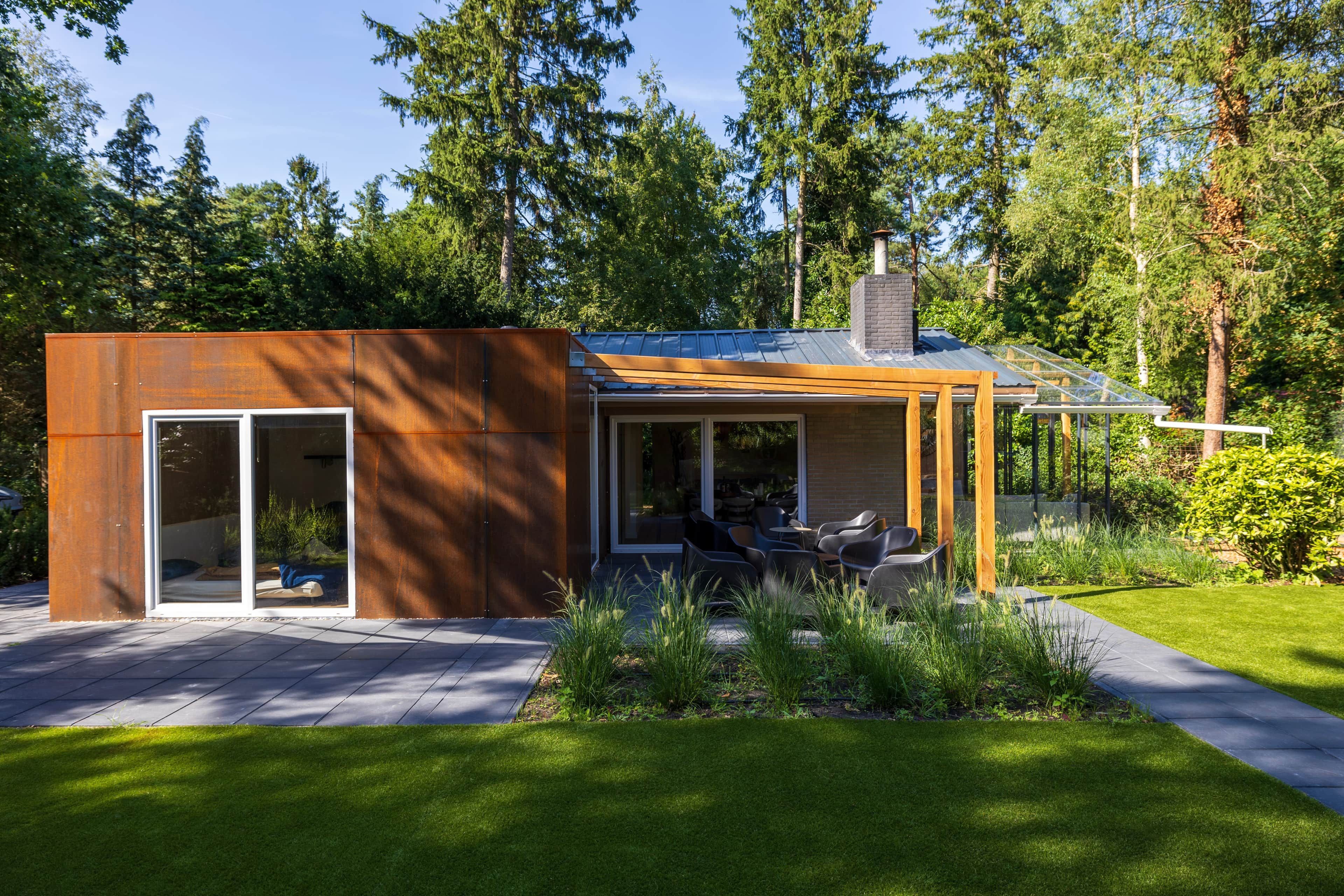 Ein modernes Haus mit Glastür, einer Terrasse mit Sitzgelegenheiten und einem Garten.