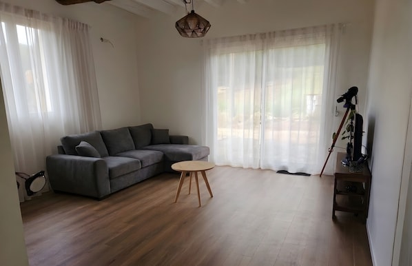 Un salon avec un canapé gris, une table ronde en bois et un appareil photo posé sur un trépied.