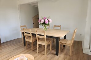 A dining area with a wooden table and chairs, a vase with flowers, and a wooden floor. - Holiday Home 'Mendi Borda' with Private Terrace, Wi-Fi and Air Conditioning (Larribar-Sorhapuru)