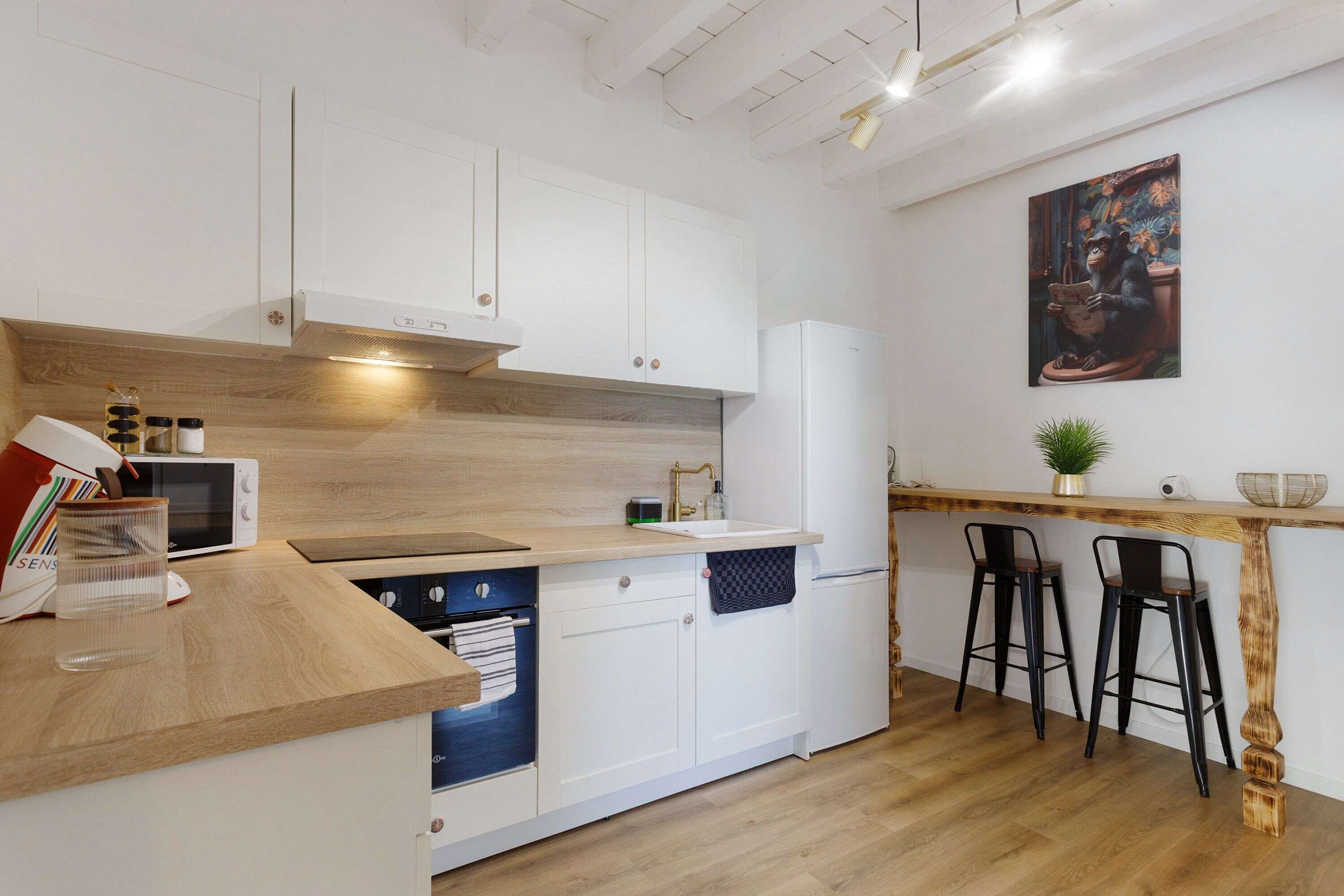 Een moderne keuken met witte kastjes, een houten aanrecht, een magnetron, een spoelbak en een barstoel.