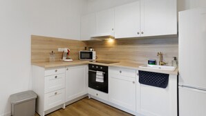 Cocina compacta con armarios blancos, un microondas, un lavamanos y un pequeño bote de basura.
