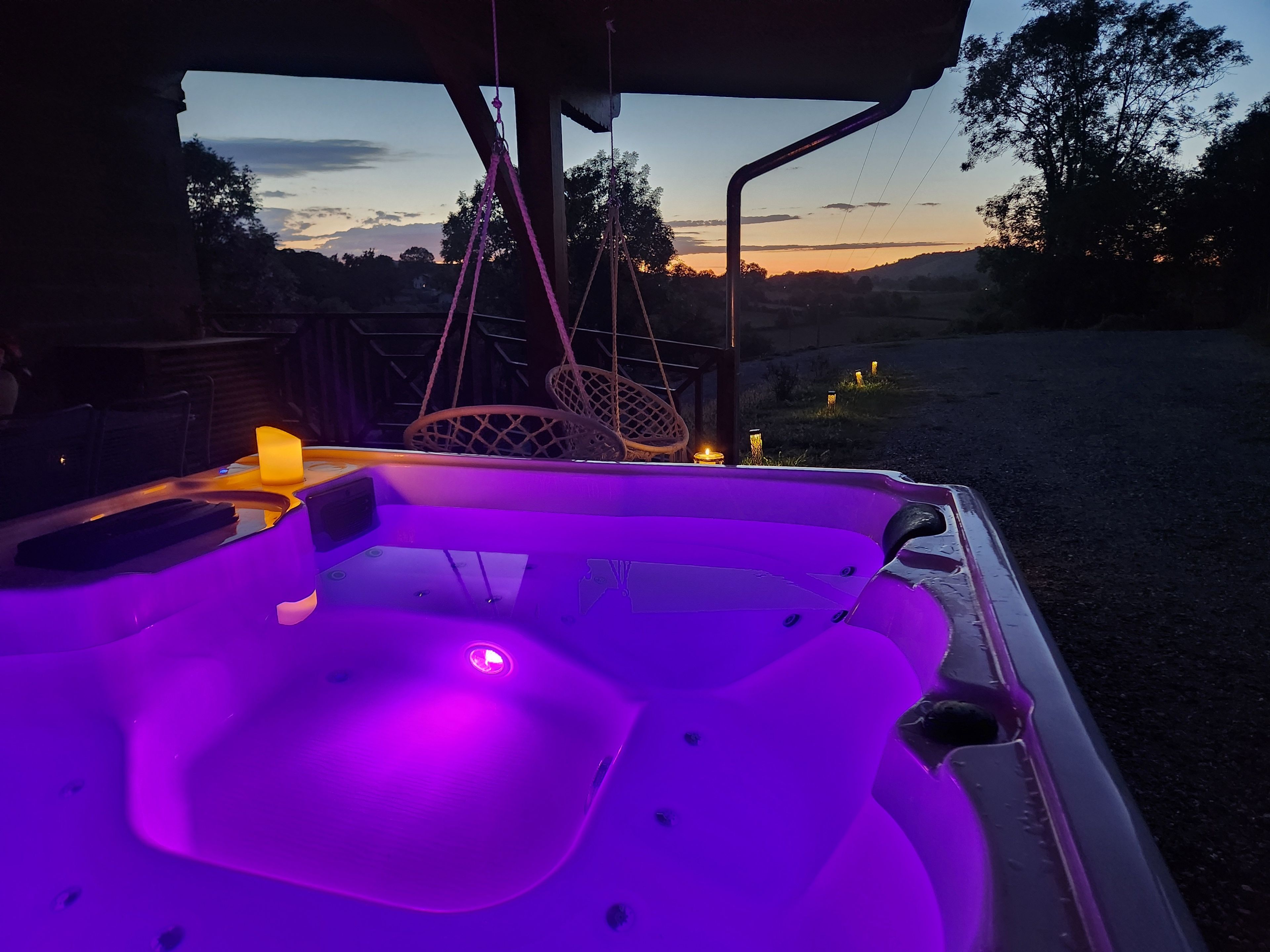 Een bubbelbad met paars licht, omringd door zitplaatsen buiten en een uitzicht op het landschap.
