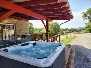 A hot tub under a covered patio with a view of a rural landscape.