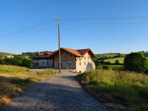 Une maison de campagne avec une allée en gravier, entourée de verdure et de collines.