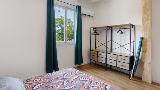 Un dormitorio con una cama, un tocador, una ventana con cortinas y una estructura de madera.
