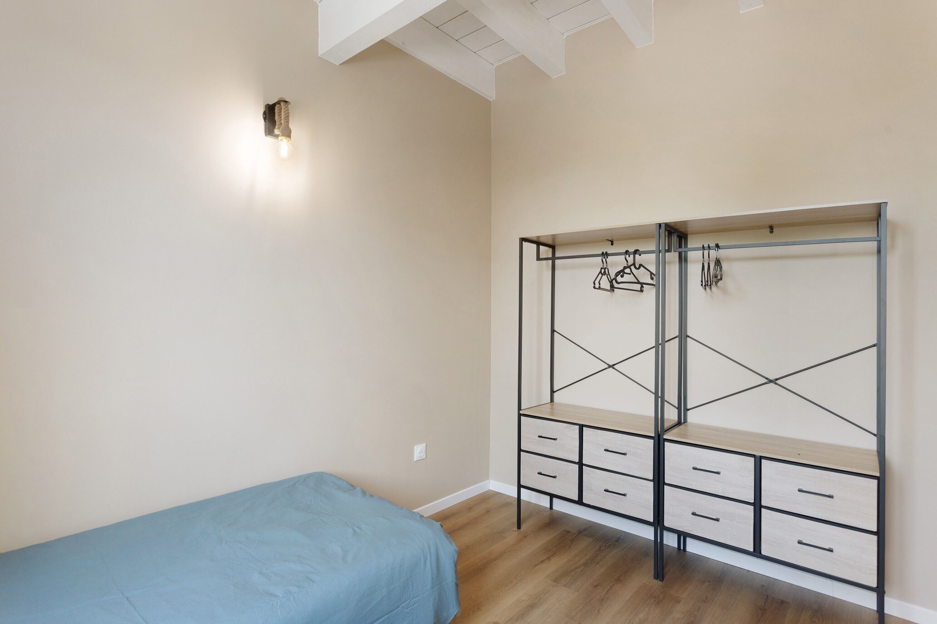 A bedroom with a bed, a wardrobe with multiple drawers, and a wall-mounted light fixture.