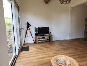 Une pièce avec un plancher en bois, un téléviseur posé sur un meuble en bois, un trépied avec un appareil photo et une bougie sur un plateau.