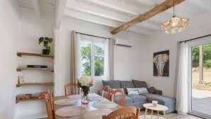 Comedor con una mesa de madera, sillas y un jarrón de flores. Hay un sofá gris y un cuadro en la pared.