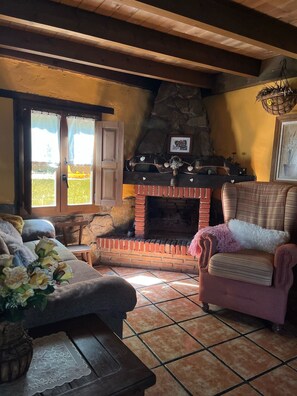 Una sala de estar acogedora con chimenea, una pared de piedra y una ventana con cortinas.