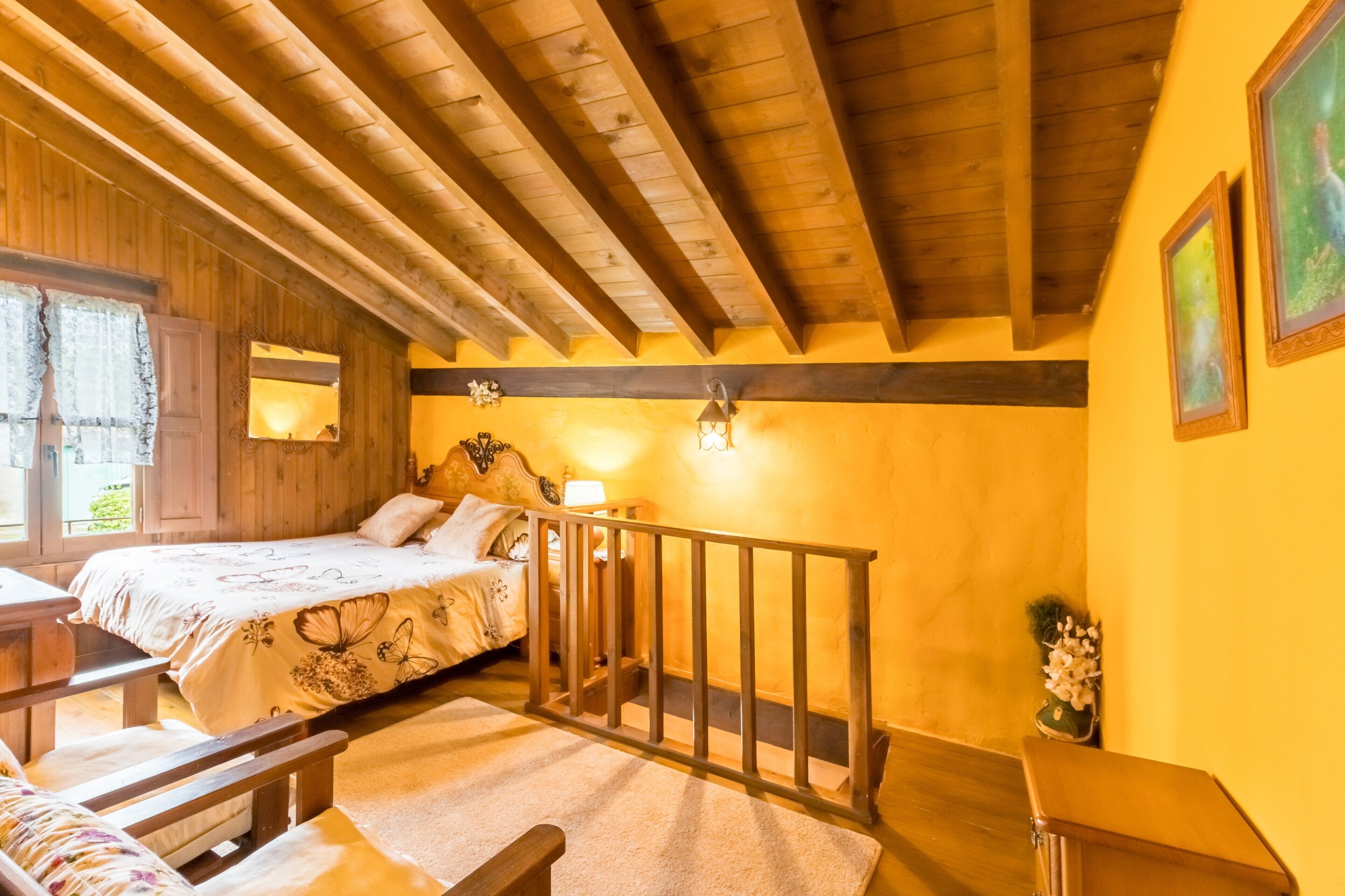 A cozy room with a bed, wooden ceiling beams, a small table, and a bench.