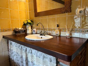 Un baño con tocador de madera, lavamanos, espejo y un revestimiento de pared de azulejos decorativos.
