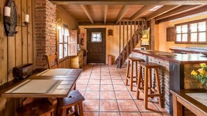 A rustic interior with wooden beams, a brick wall, a kitchen area, and a dining space with tables and chairs.