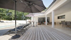 Um deck de madeira com mobiliário externo, piscina e um espaço coberto com varanda.
