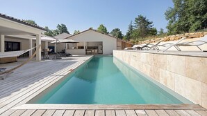 Uma piscina com deck de madeira, espreguiçadeiras e área de estar coberta.