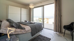 Quarto com cama, cadeira, mesa de cabeceira, janela grande e vista para o exterior.