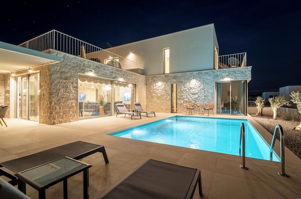 Ein modernes Haus mit Swimmingpool, Natursteinaußenwand und Balkon mit Sitzgelegenheit.