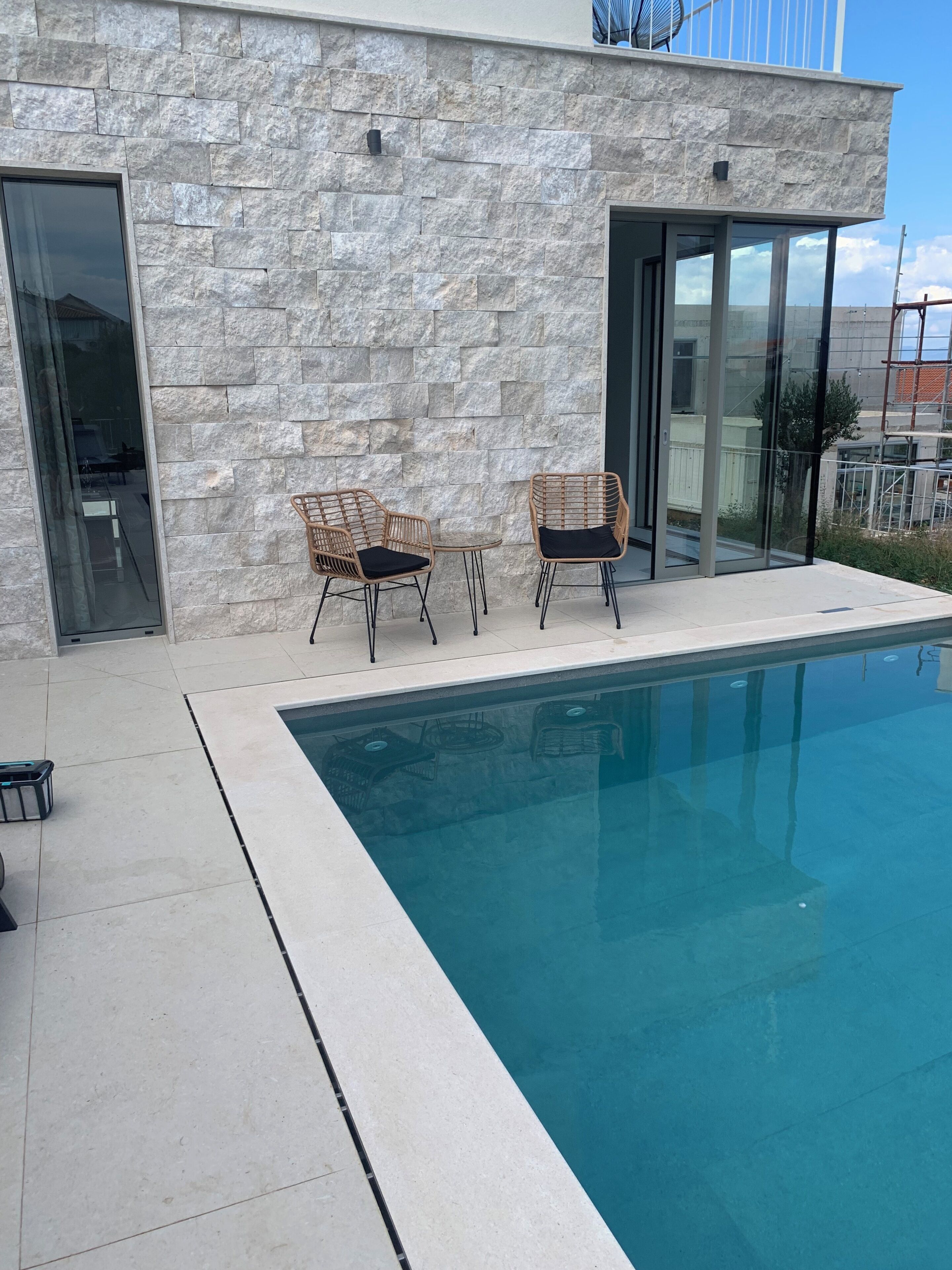 A modern building with a stone facade, a swimming pool, and two wicker chairs.