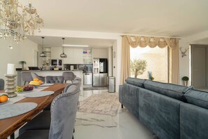 Ein modernes Wohnzimmer mit Sofa, Esstisch, einer Kandelaberleuchte und einer Küche im Hintergrund.