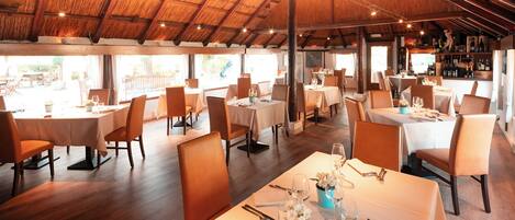 A restaurant with multiple tables and chairs, a wooden ceiling, and a view of the outdoors.