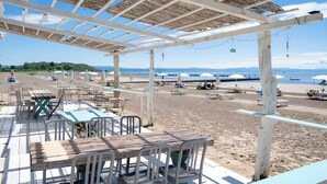 Um restaurante à beira-mar com área externa, telhado de palha e vista para a praia e o mar.