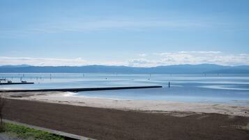 Ein Strand mit einer hölzernen Pier, die sich über ruhiges Wasser erstreckt, einem klaren Himmel und fernen Bergen.