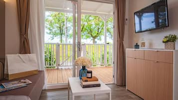 Una habitación moderna con sofá, una mesita con libros, televisor montado en la pared y puerta corrediza de vidrio que da a una terraza exterior.