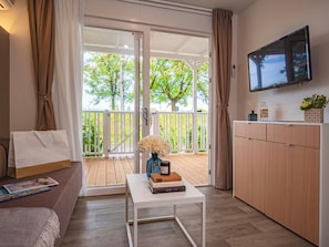 Ein modernes Zimmer mit einer Couch, einem kleinen Tisch mit Büchern, einem an der Wand befestigten Fernseher und einer Glastür zum Außenbereich.