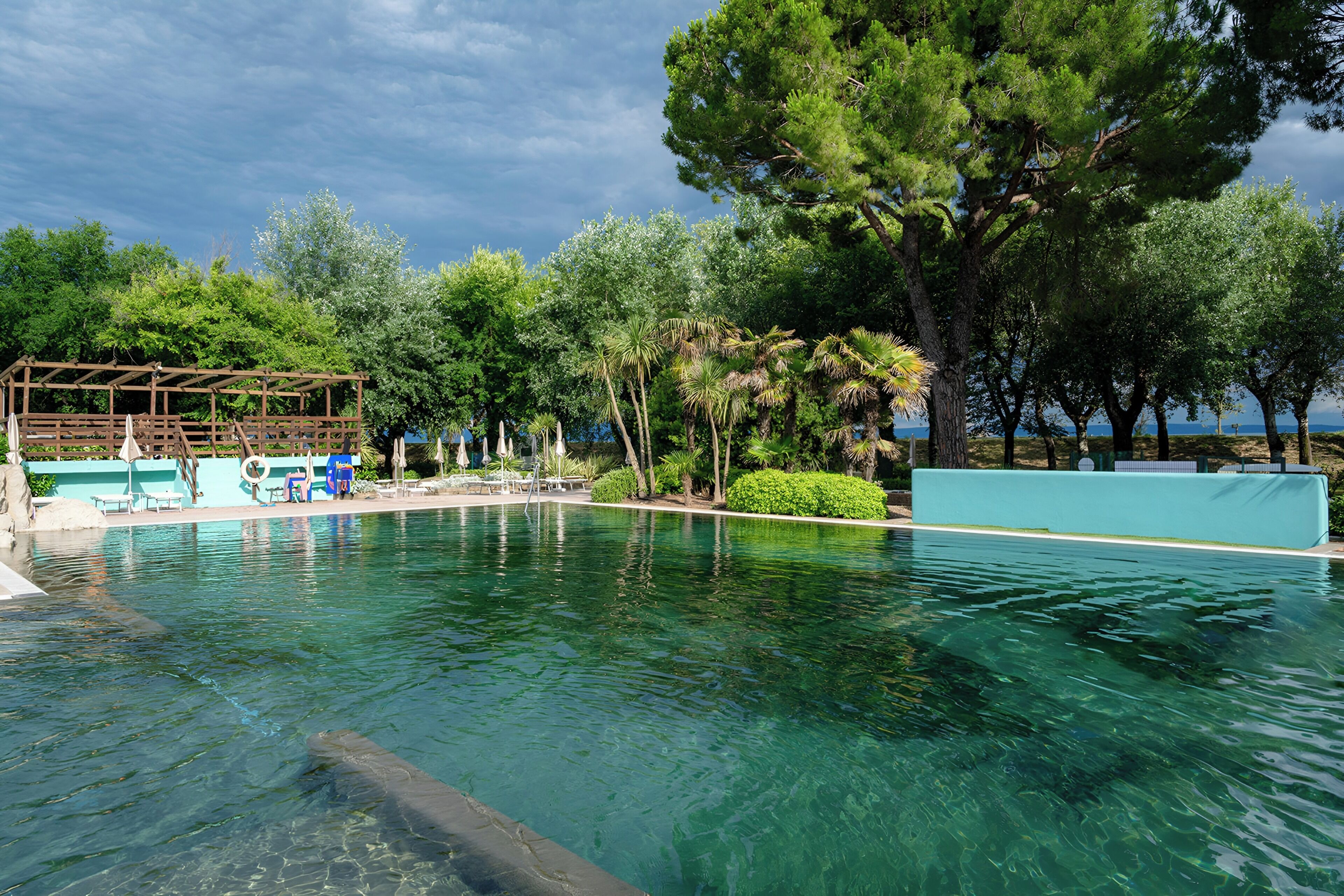A clear swimming pool with lounge chairs and a wooden pergola.