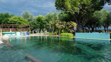 A clear swimming pool with lounge chairs and a wooden pergola.