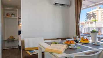 A hotel room with a dining table set with breakfast, a bookshelf, and a view of a building with balconies.