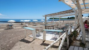 Um restaurante à beira-mar com mesas ao ar livre, guarda-sóis e vista para o mar.
