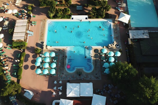 Vista aérea de un área de piscina con varias piscinas, tumbonas, sombrillas y sillones de relax.