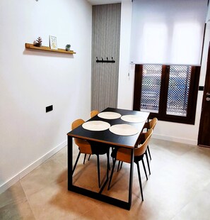 Un'area pranzo con un tavolo nero e sedie di legno, una piccola mensola con oggetti decorativi, una finestra con vista e una porta con zanzariera.