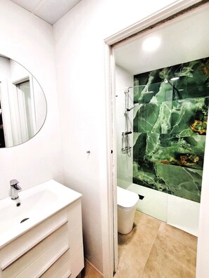 Un baño con tocador blanco, espejo, ducha con puerta de vidrio y salpicadero de mármol.