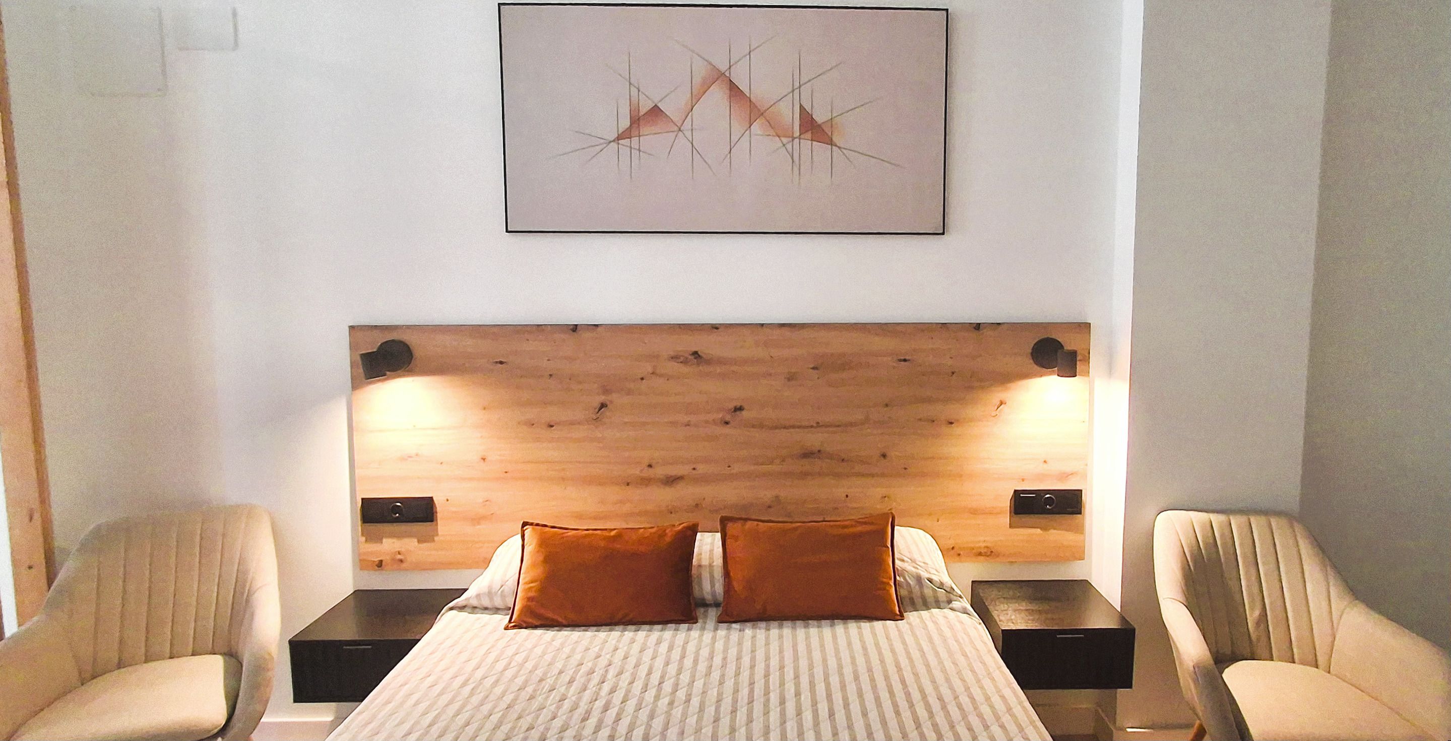 Habitació d'hotel amb un panell de fusta al capçal del llit, dues taules de nit, un llit amb un edredó a ratlles, dos coixins i una obra d'art abstracta penjada a la paret.