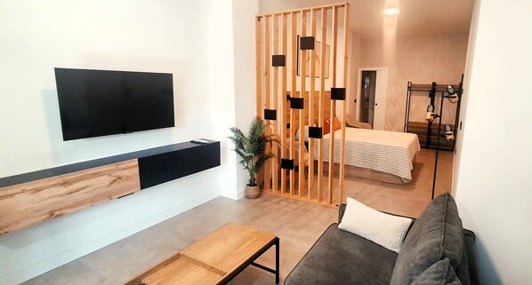 Una sala de estar moderna con un televisor de pantalla plana, una mesa de centro de madera, un sofá gris y una planta grande en maceta.
